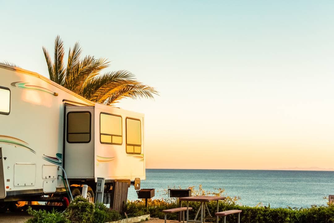 Motorhome by the beach at sunset with palms and a picnic table