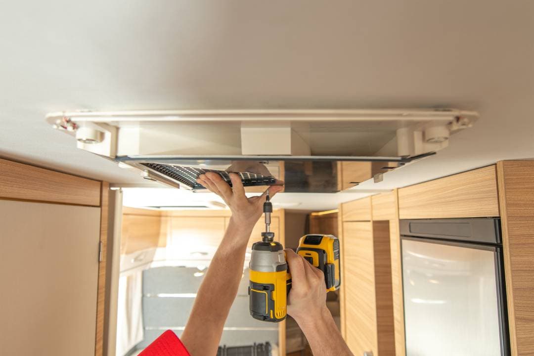 Technician using a power drill to work on a ceiling vent inside an RV