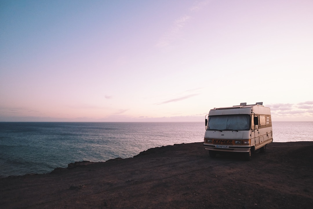 White campervan on a clifftop above the ocean at sunrise
